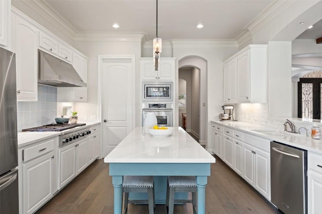 kitchen with arched walkways, a sink, under cabinet range hood, appliances with stainless steel finishes, and white cabinetry