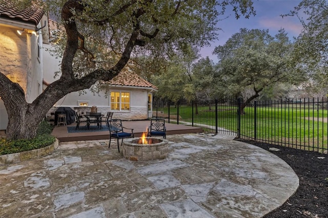 patio terrace at dusk with a fire pit, outdoor dining area, a yard, and fence