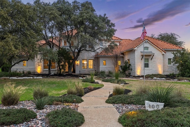 mediterranean / spanish-style home featuring a lawn, stone siding, stucco siding, and a tiled roof