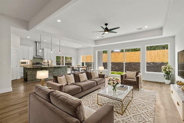 living area with a raised ceiling, recessed lighting, light wood-style floors, and visible vents