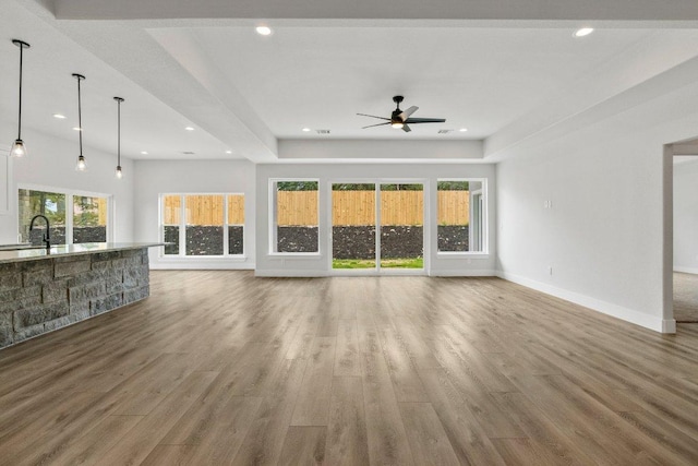 unfurnished living room featuring recessed lighting, baseboards, a raised ceiling, and wood finished floors