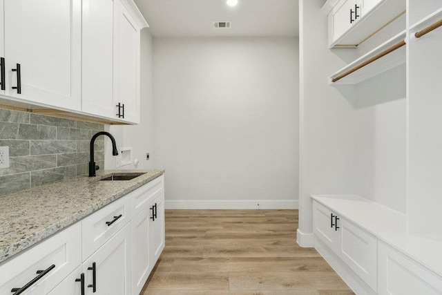 interior space with visible vents, baseboards, white cabinets, light wood-type flooring, and backsplash