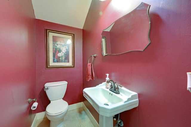 half bath featuring tile patterned floors, toilet, baseboards, and a sink