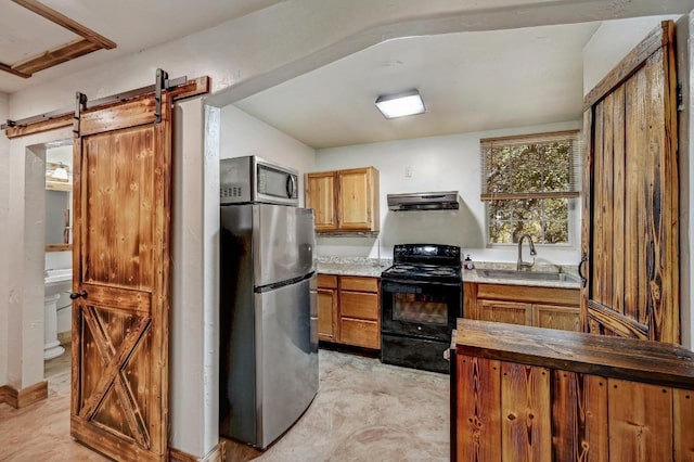 kitchen featuring a barn door, brown cabinets, appliances with stainless steel finishes, exhaust hood, and a sink