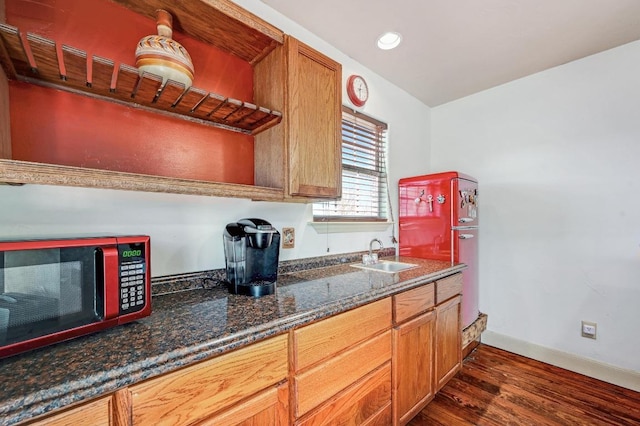 kitchen featuring a sink, dark wood finished floors, recessed lighting, dark stone counters, and baseboards