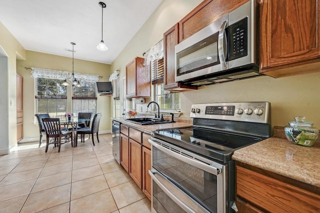 kitchen featuring decorative light fixtures, brown cabinets, light tile patterned flooring, stainless steel appliances, and a sink