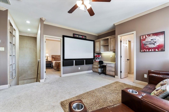 home theater with a ceiling fan, baseboards, ornamental molding, built in desk, and light carpet