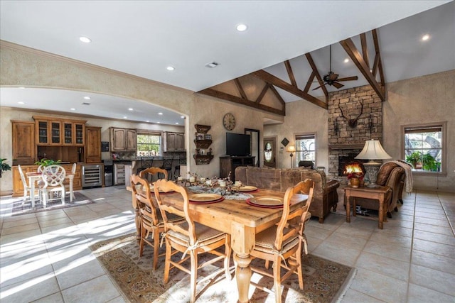 dining space with beam ceiling, a stone fireplace, plenty of natural light, and high vaulted ceiling