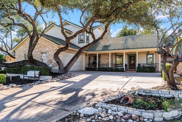 traditional home with stucco siding, driveway, stone siding, covered porch, and a garage