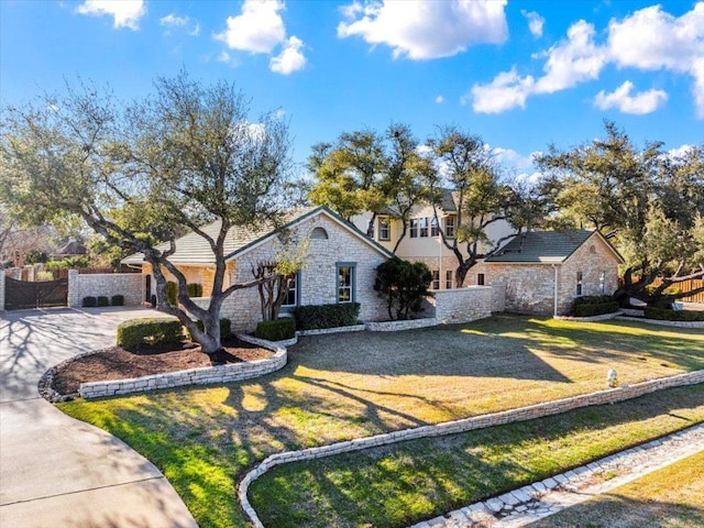 view of front of property featuring a front yard, fence, stone siding, and driveway