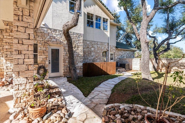 exterior space with central AC unit, stone siding, stucco siding, and fence