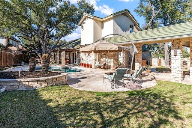 rear view of property featuring stucco siding, a lawn, stone siding, fence, and a patio area