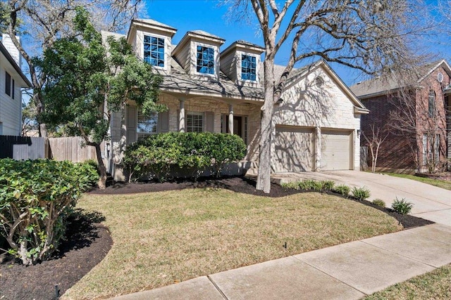 view of front of property featuring driveway, stone siding, fence, a front yard, and a garage