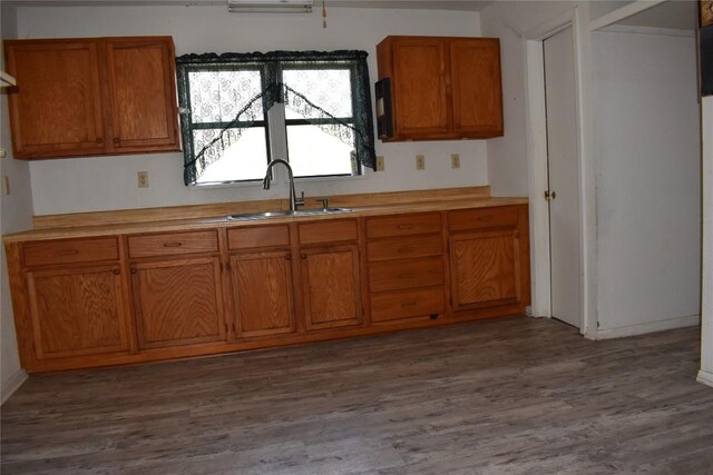 kitchen featuring light countertops, brown cabinets, dark wood-style flooring, and a sink