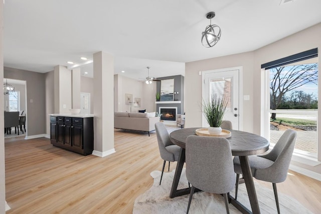 dining area with recessed lighting, a lit fireplace, light wood finished floors, baseboards, and a chandelier