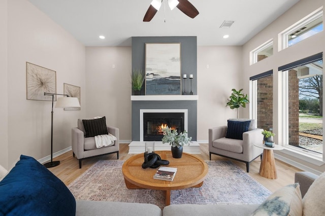 living room featuring a glass covered fireplace, recessed lighting, wood finished floors, and visible vents