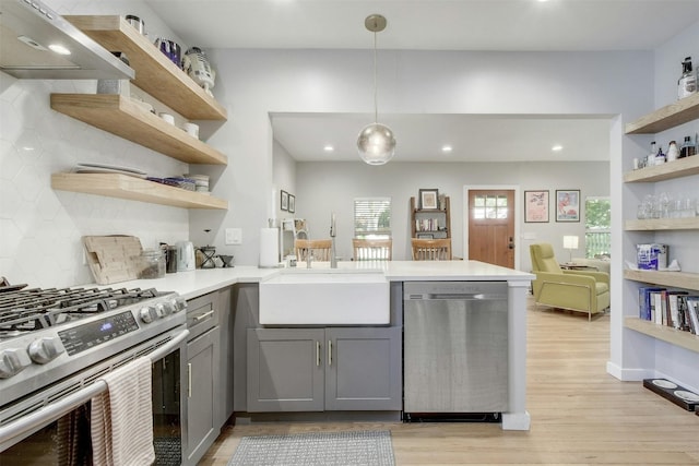 kitchen featuring gray cabinets, open shelves, a sink, stainless steel appliances, and a peninsula