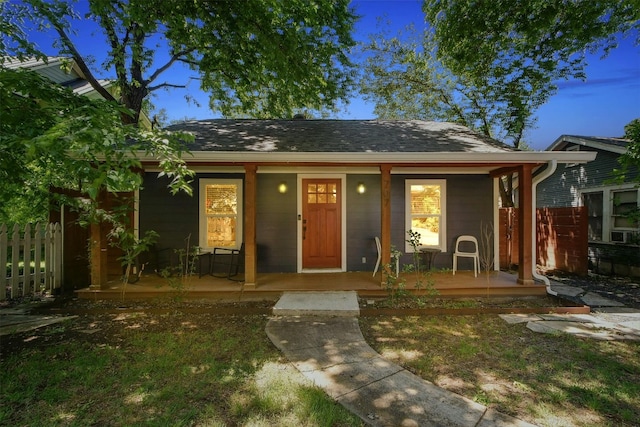 view of front of home with covered porch, a shingled roof, and fence