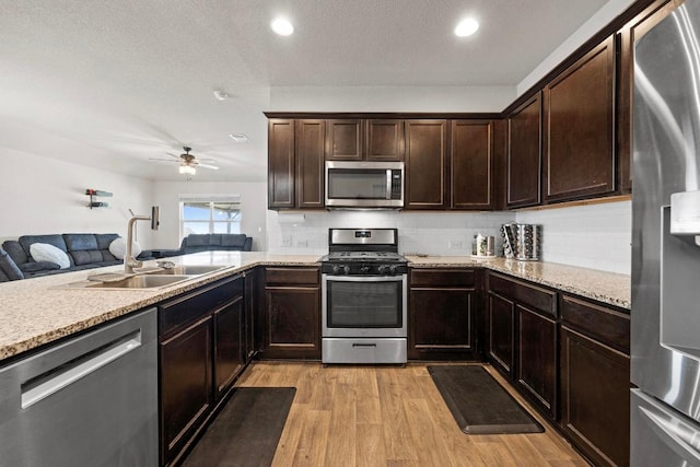 kitchen featuring light wood-type flooring, a sink, dark brown cabinetry, appliances with stainless steel finishes, and open floor plan