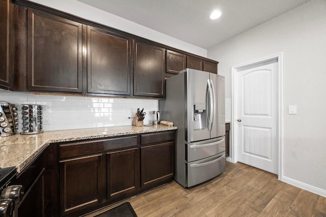 kitchen featuring decorative backsplash, dark brown cabinets, wood finished floors, and stainless steel fridge