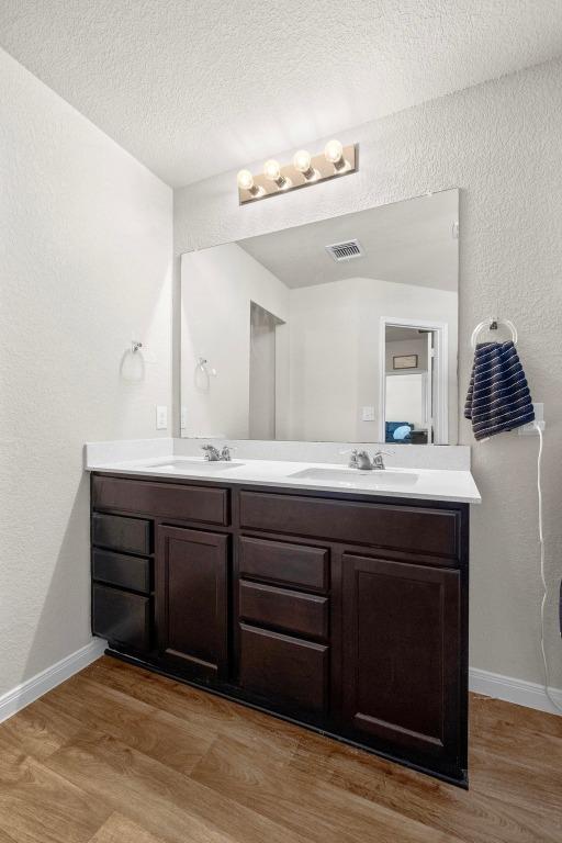 bathroom featuring double vanity, wood finished floors, visible vents, and a sink