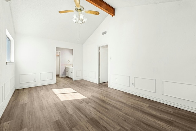 unfurnished bedroom with visible vents, connected bathroom, vaulted ceiling with beams, wood finished floors, and a decorative wall