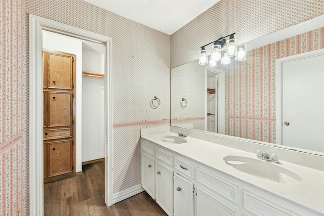 bathroom with wood finished floors, wallpapered walls, and a sink