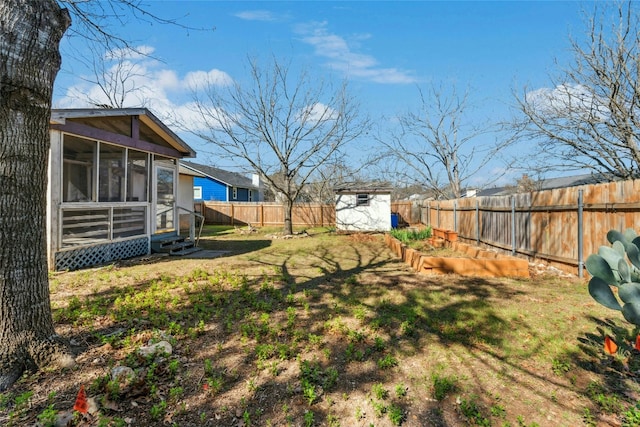 view of yard featuring a fenced backyard, a shed, a vegetable garden, an outdoor structure, and a sunroom