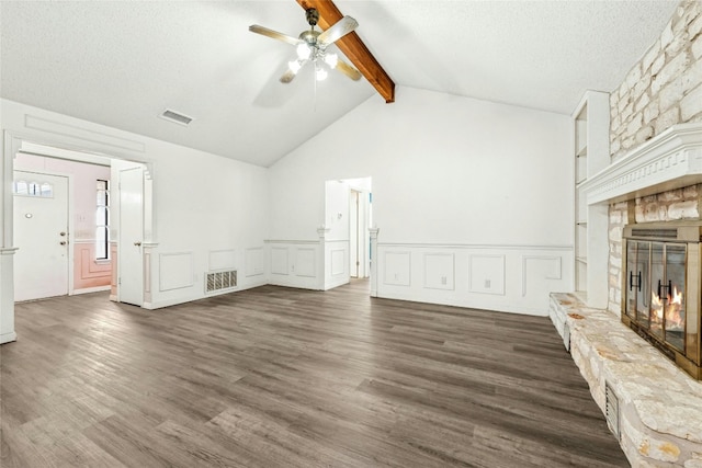 unfurnished living room featuring visible vents, dark wood finished floors, vaulted ceiling with beams, a stone fireplace, and a textured ceiling