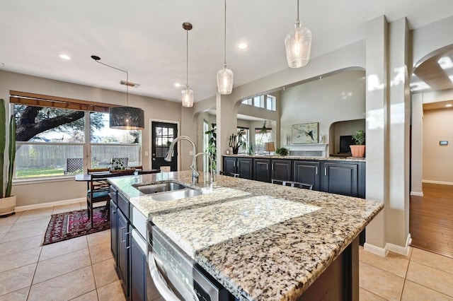 kitchen with a sink, light stone counters, decorative light fixtures, light tile patterned floors, and baseboards