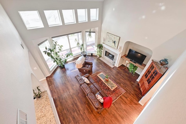 living room featuring a towering ceiling, wood finished floors, and a tiled fireplace