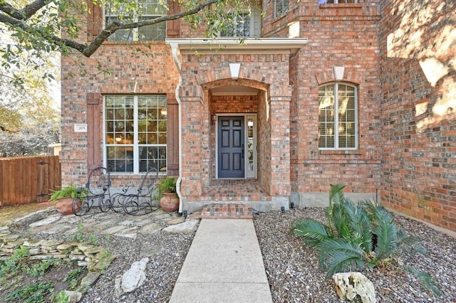 view of exterior entry with fence and brick siding