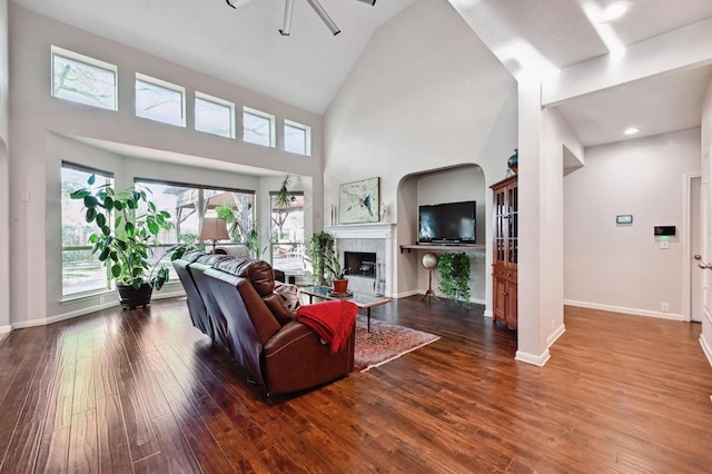 living area with baseboards, high vaulted ceiling, wood finished floors, and a tile fireplace