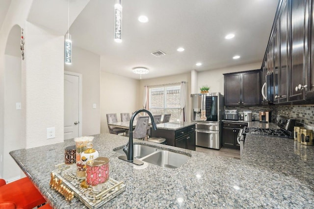 kitchen featuring visible vents, a sink, stone countertops, appliances with stainless steel finishes, and decorative backsplash