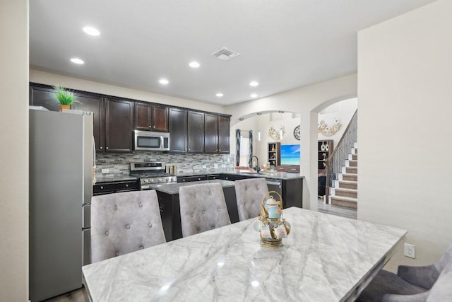 kitchen with a sink, a center island, appliances with stainless steel finishes, decorative backsplash, and dark brown cabinets