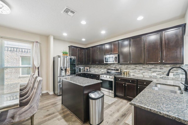 kitchen featuring a sink, light stone counters, stainless steel appliances, light wood finished floors, and decorative backsplash