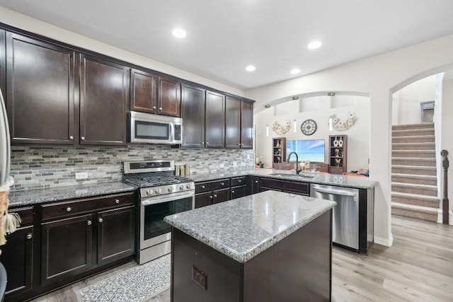 kitchen with a sink, light stone counters, a kitchen island, stainless steel appliances, and decorative backsplash