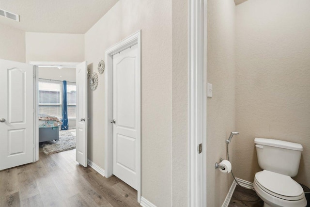 bathroom featuring toilet, wood finished floors, visible vents, and baseboards