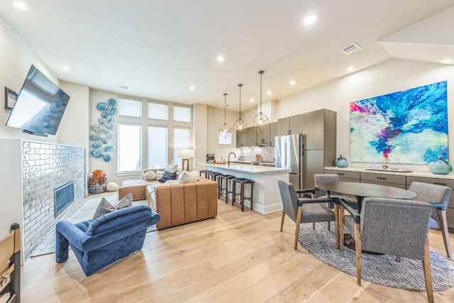 living area with visible vents, high vaulted ceiling, a brick fireplace, and light wood finished floors