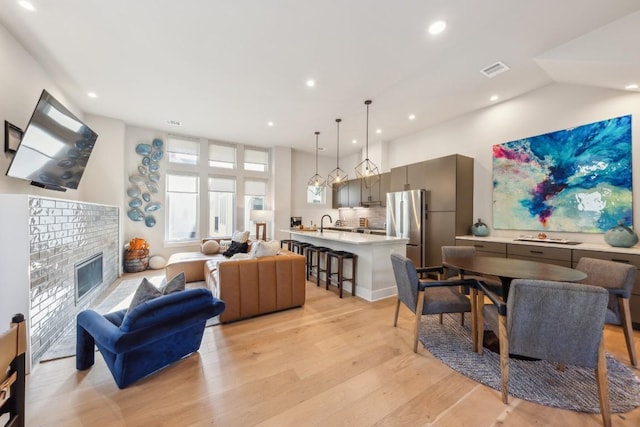 living area featuring visible vents, recessed lighting, light wood finished floors, a brick fireplace, and vaulted ceiling