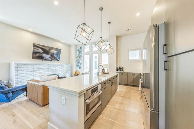 kitchen with visible vents, modern cabinets, an island with sink, open floor plan, and stainless steel appliances