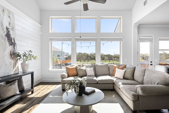 living room featuring visible vents, baseboards, ceiling fan, a towering ceiling, and wood finished floors