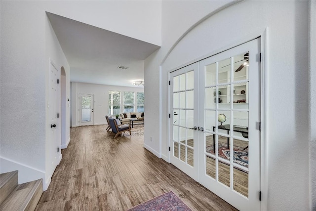 corridor featuring visible vents, baseboards, french doors, wood finished floors, and arched walkways