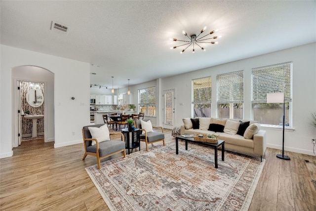 living room with an inviting chandelier, visible vents, arched walkways, and light wood finished floors