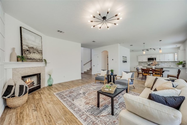 living area featuring visible vents, light wood-style flooring, a warm lit fireplace, arched walkways, and stairs