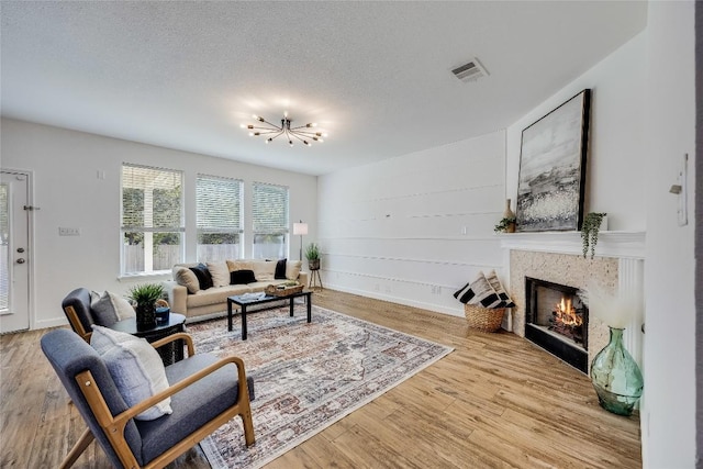 living room featuring visible vents, a notable chandelier, a textured ceiling, wood finished floors, and a tile fireplace