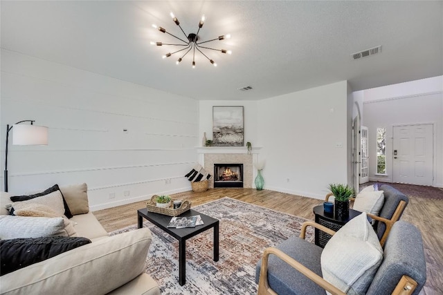 living room with wood finished floors, visible vents, a chandelier, and a lit fireplace