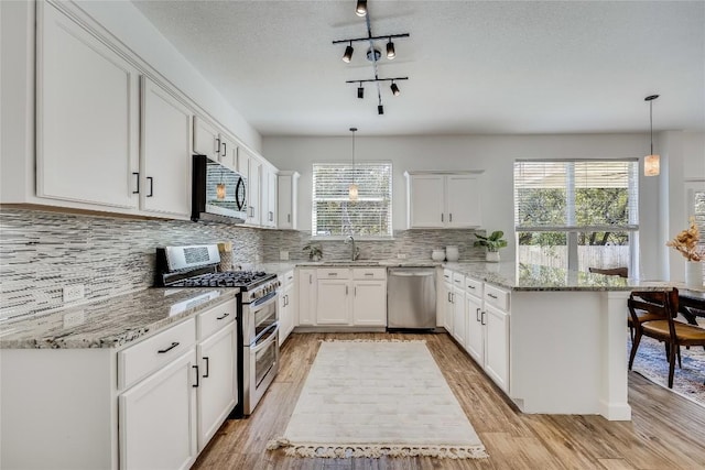 kitchen with a peninsula, light wood-style flooring, stainless steel appliances, white cabinetry, and backsplash