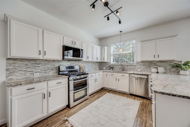 kitchen with light stone counters, appliances with stainless steel finishes, white cabinetry, light wood-type flooring, and backsplash