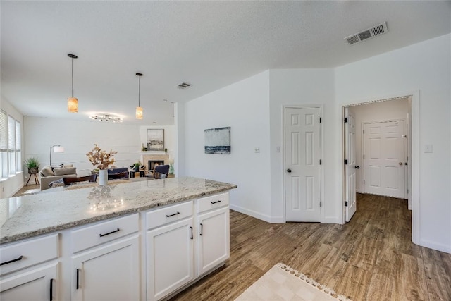 kitchen with a fireplace, light wood-style floors, visible vents, and white cabinetry